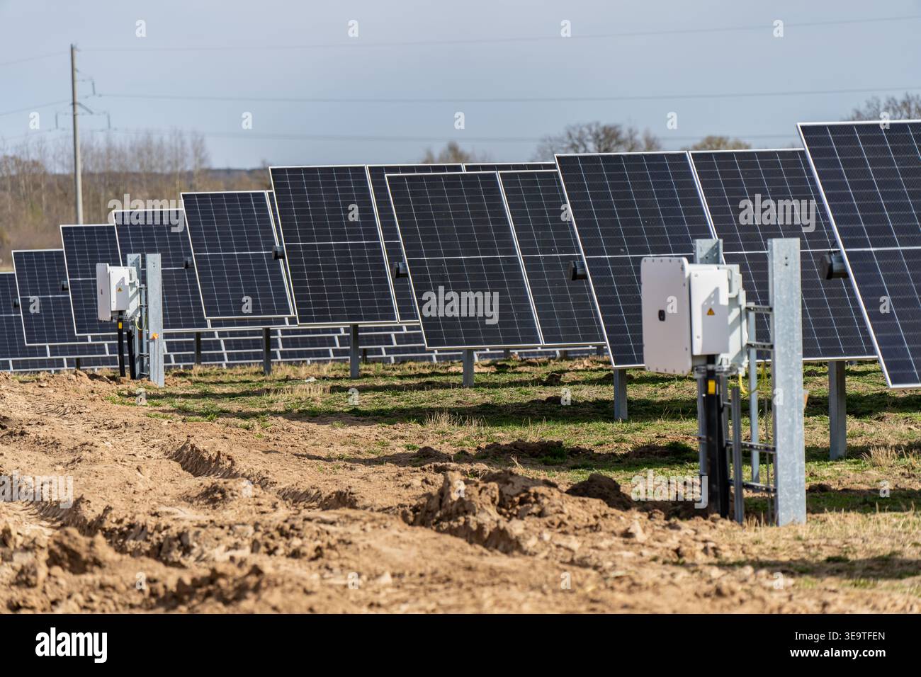 Ampie file di pannelli solari industriali con scatole di inverter elettrici su sistemi di tracciamento in un campo rurale per la produzione di energia rinnovabile e la sostenibilità Foto Stock