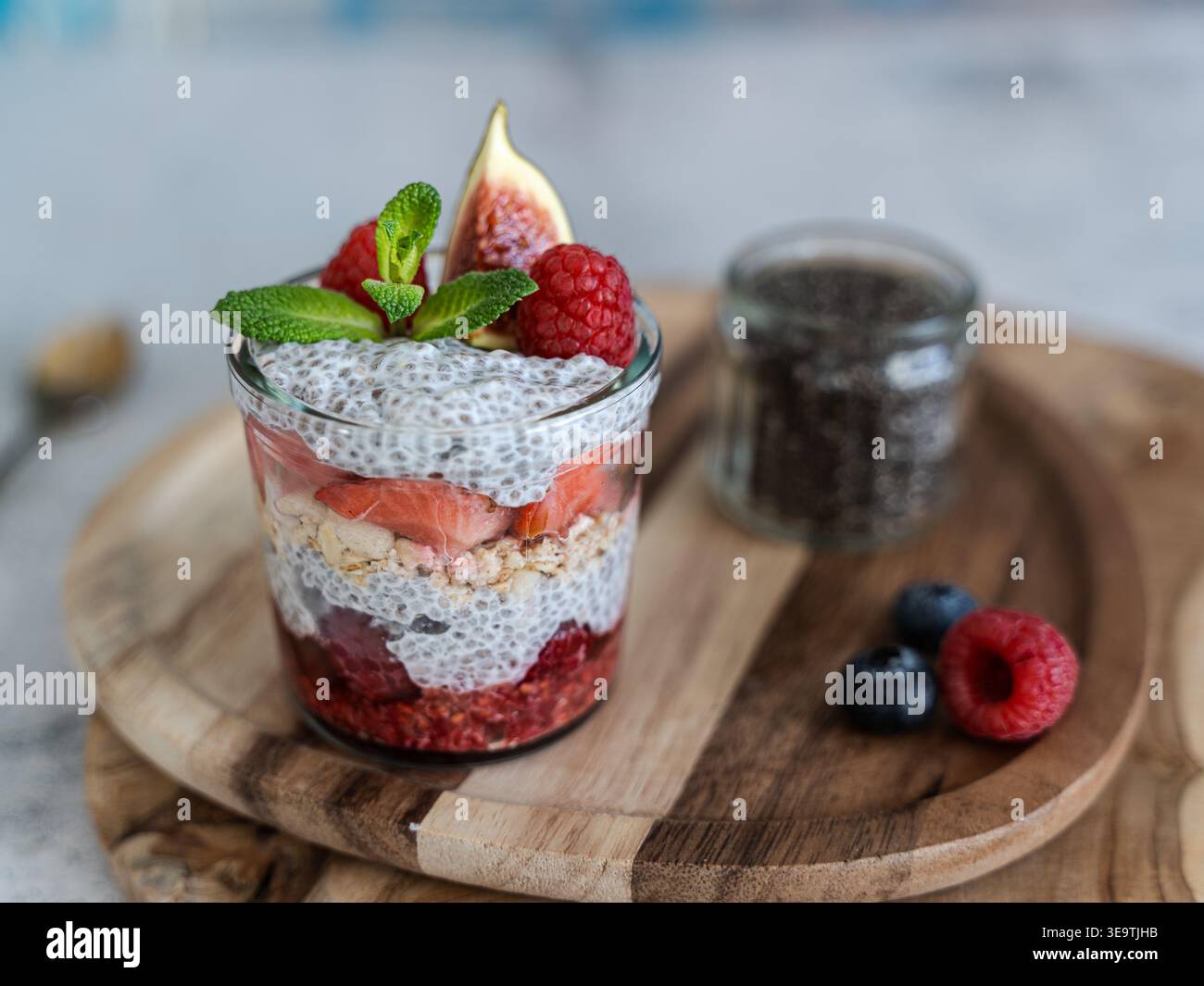 Vista frontale del chia parfait con frutti di bosco menta e granola su tavola di legno dai toni naturali Foto Stock