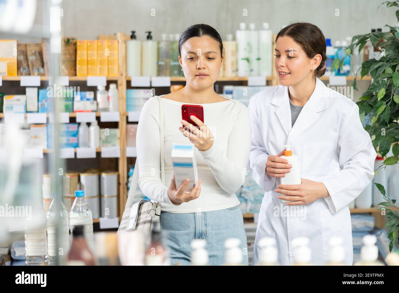 Cliente donna che esegue la scansione del codice QR sulla crema per il corpo in farmacia Foto Stock