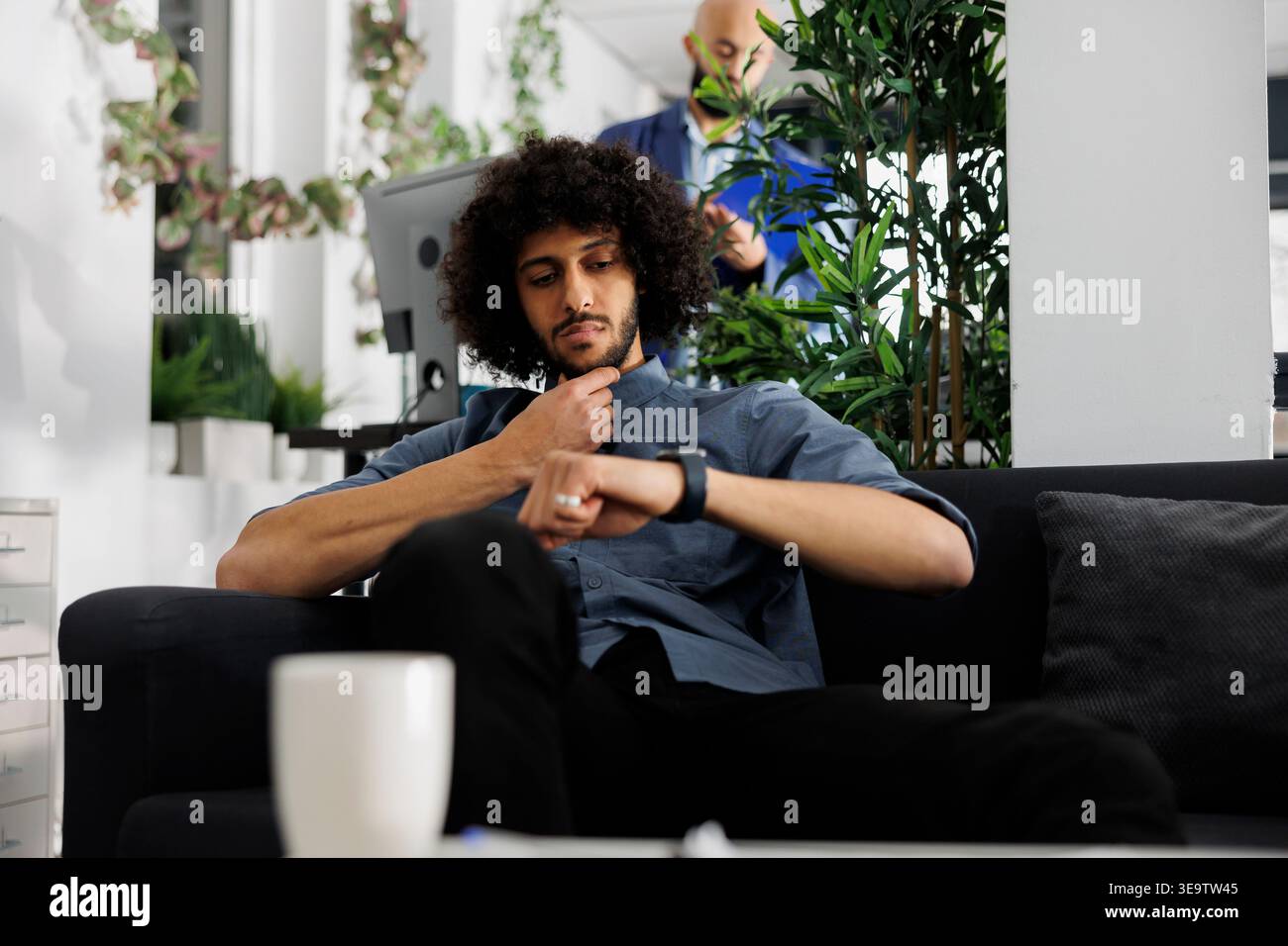 Imprenditore arabo attento che controlla il programma di lavoro sullo smartwatch in ufficio. Calendario di pianificazione pensivo con orologio elettronico per rispettare la scadenza del progetto mentre si è seduti nello spazio di coworking Foto Stock