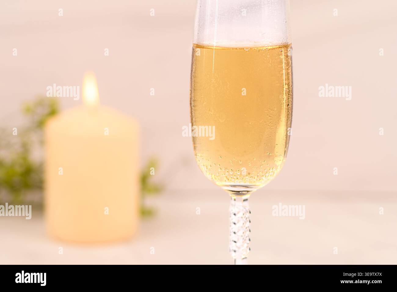 Bicchiere di champagne con dietro la candela offuscata, luce soffusa e romantica e atmosfera tranquilla. Foto Stock