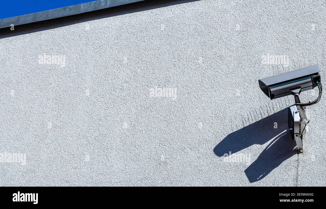 Telecamera di sorveglianza di sicurezza montata su una parete dell'edificio che proietta ombra alla luce del sole, concetto di sicurezza minimalista con spazio di copia. Foto Stock