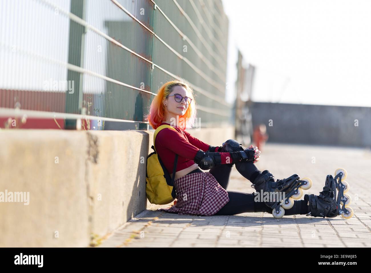 Una giovane donna che sta appoggiando a terra contro la recinzione Foto Stock