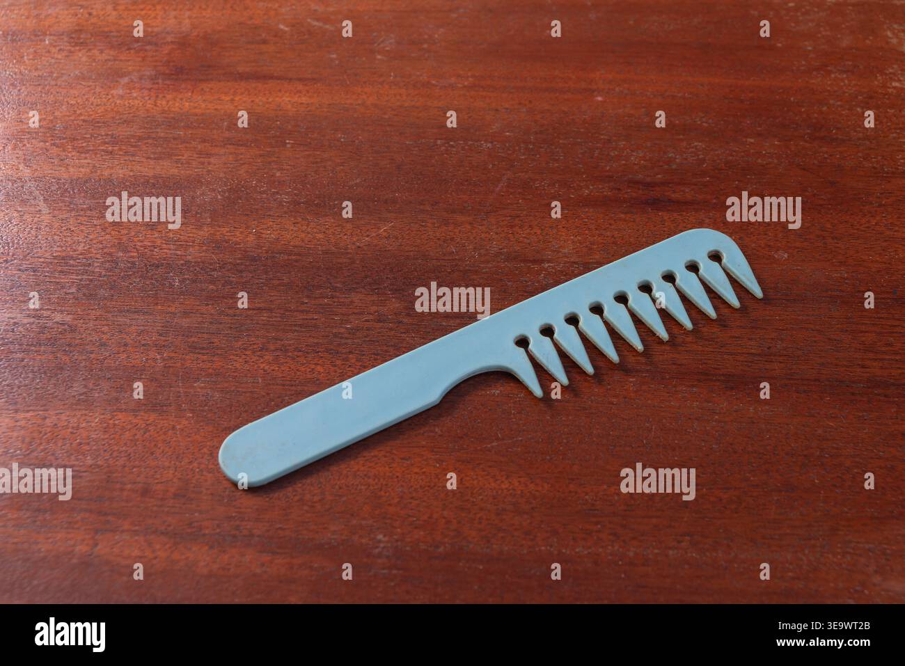 Il pettine poggia sulla superficie in legno. Illuminazione soffusa, ombre minime. La venatura del legno è visibile e ruvida. Immagine ideale per la cura dei capelli, concetti di igiene personale. Foto Stock