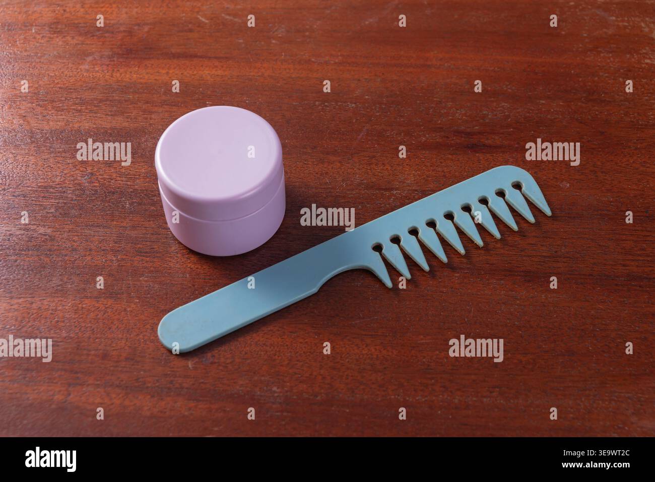 Primo piano presenta il vaso in crema lavanda e il pettine blu sulla superficie di legno. La luce soffusa e diffusa evidenzia le texture. Il concetto si concentra su cura della pelle, cura del corpo, p Foto Stock