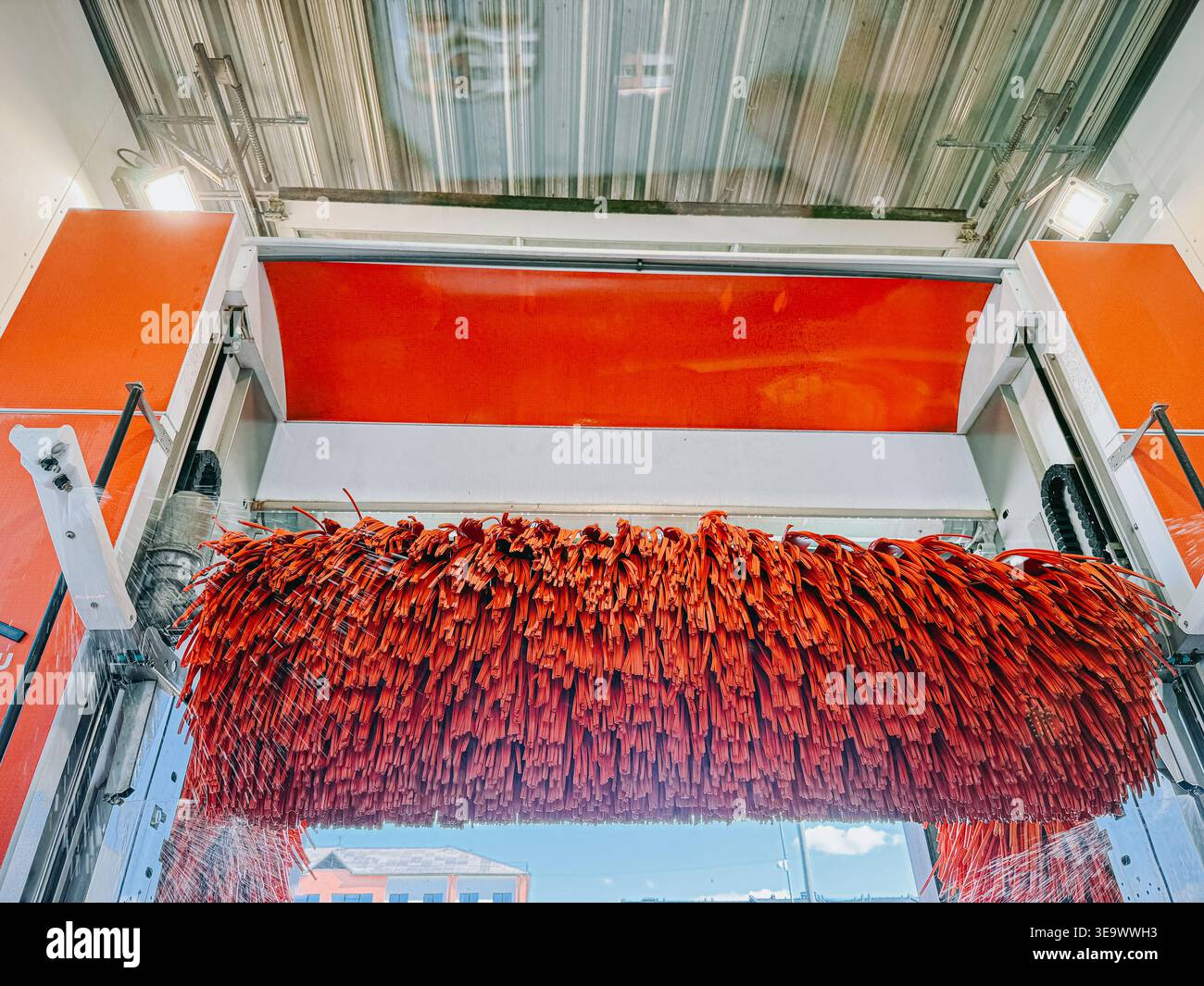 Valmiera, Lettonia - 18 aprile 2026: Vista dinamica di un tunnel di autolavaggio automatico con grandi spazzole rosse rotanti e spruzzi d'acqua in azione. Ideale per au Foto Stock