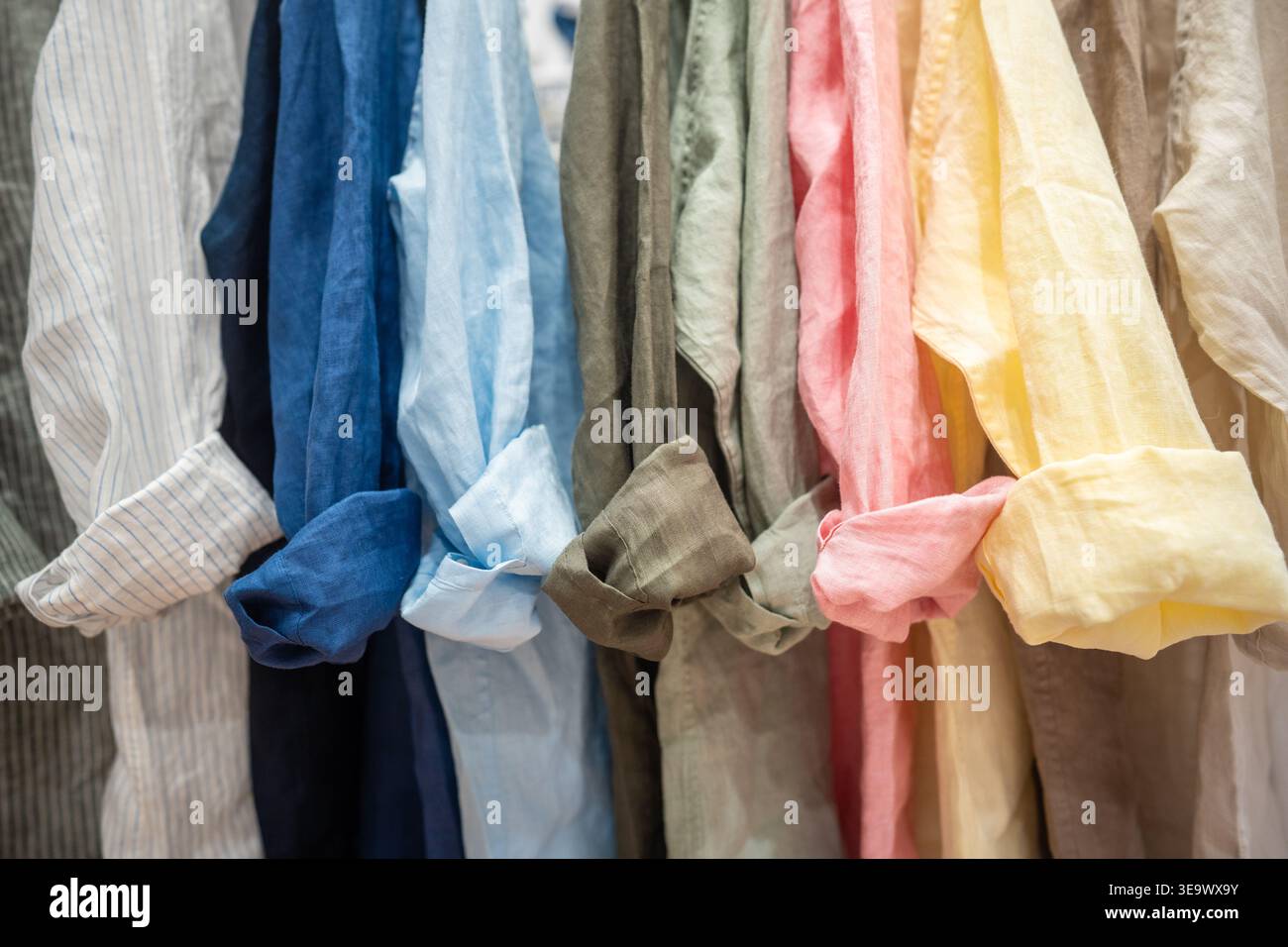Ampia gamma di camicie colorate di lino appese in esposizione presso lo showroom di un negozio di abbigliamento alla moda. Foto Stock
