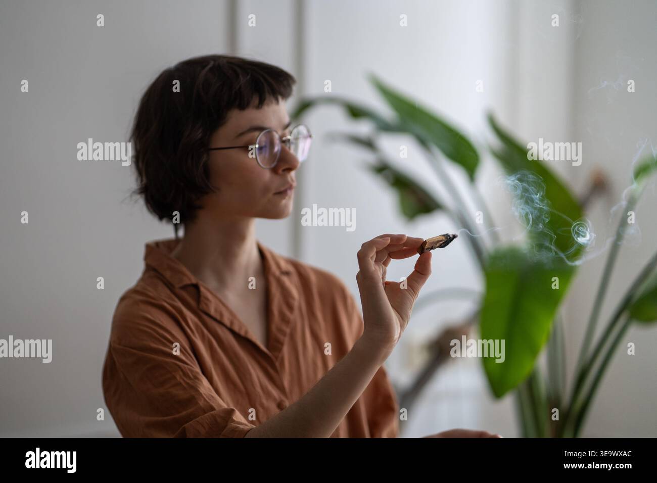 Donna rilassata che pratica cura di sé e rituali di salute mentale, alleggerisce palo santo bastone in appartamento Foto Stock