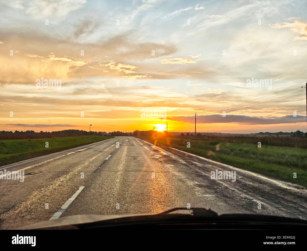 L'auto percorre una strada limpida con un tramonto sullo sfondo che mostra splendidi colori alla fine della giornata. Foto Stock