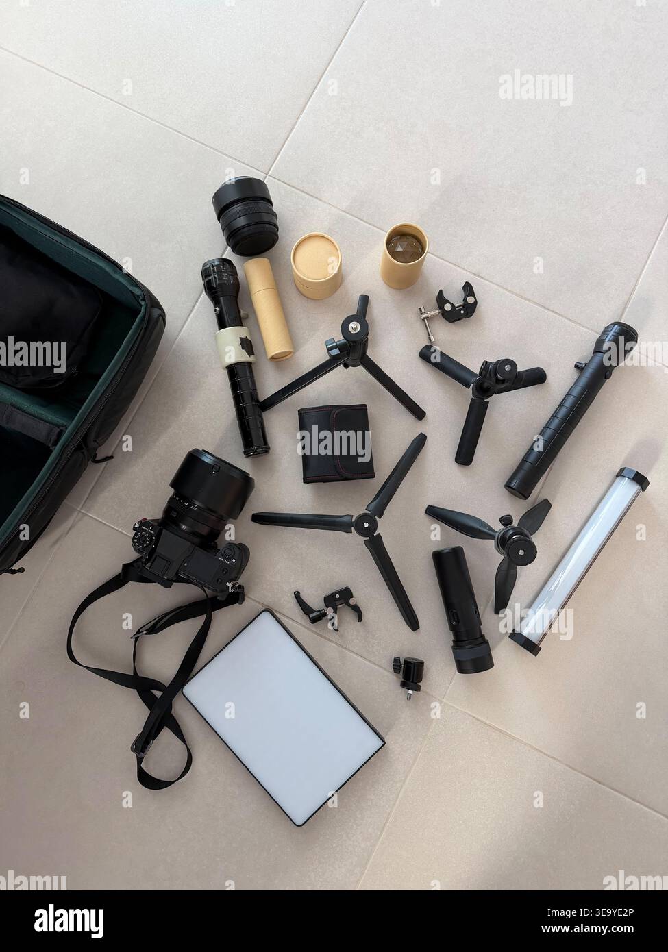 Vista dall'alto delle attrezzature fotografiche, tra cui fotocamera mirrorless, diversi mini cavalletti, pannelli luminosi a LED, lenti e torce disposte su piastrelle luminose Foto Stock