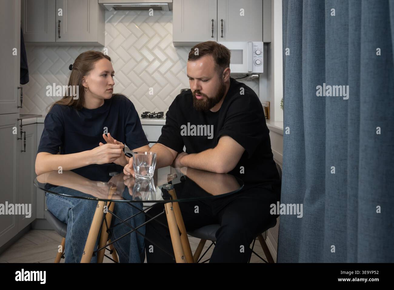 Una giovane coppia si siede al tavolo della cucina in una casa moderna, visibilmente sconvolta e parla attraverso un serio conflitto di relazioni, una conversazione emotiva e tesa Foto Stock