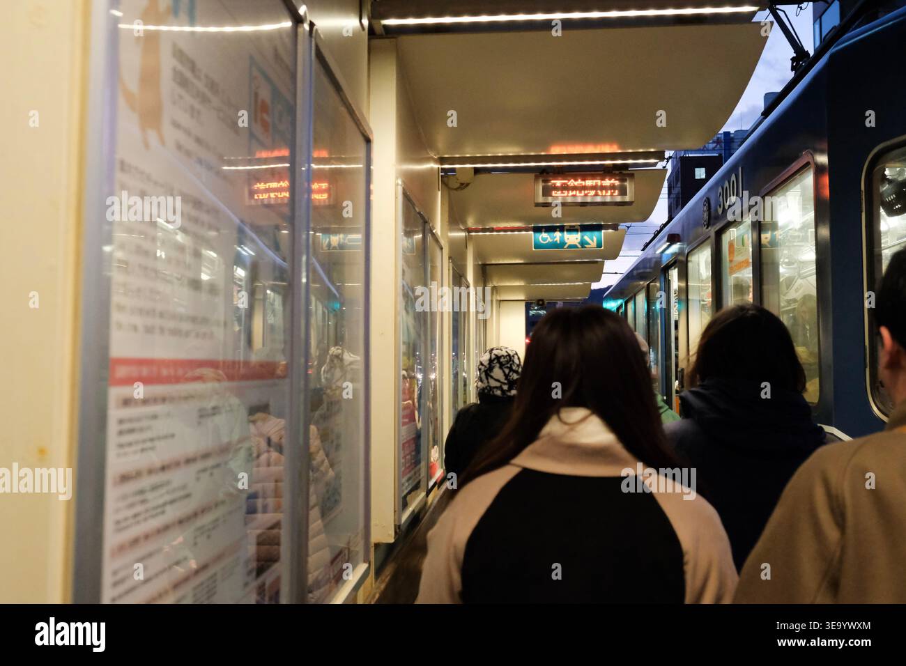 I passeggeri attendono su una piattaforma ferroviaria illuminata in Giappone Foto Stock