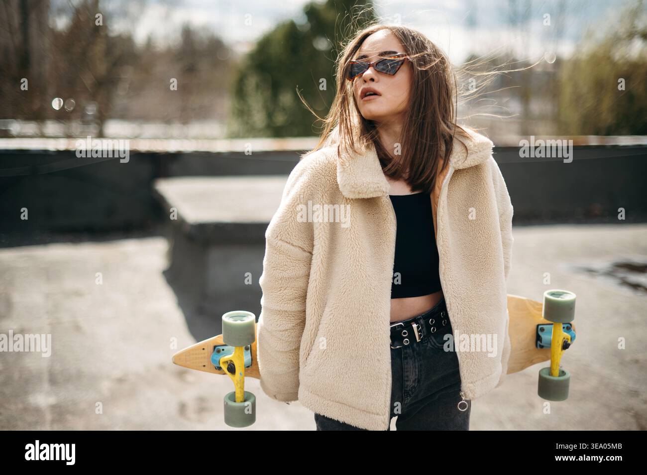 Bella donna con skateboard in piedi sul tetto dell'edificio Foto Stock