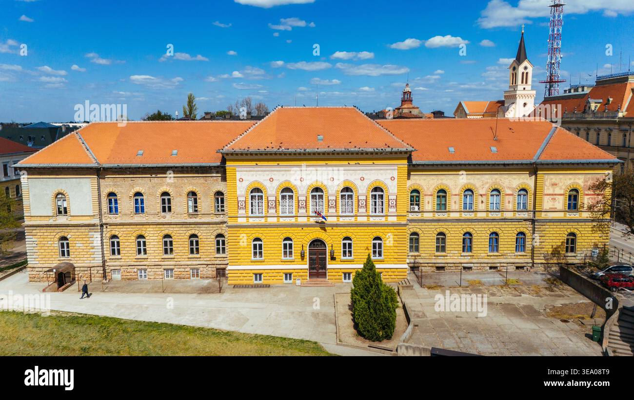 Veduta aerea della facciata gialla luminosa di un edificio, in contrasto con il tetto in terracotta e il cielo blu, Zrenjanin, Vojvodina, Serbia. Foto Stock