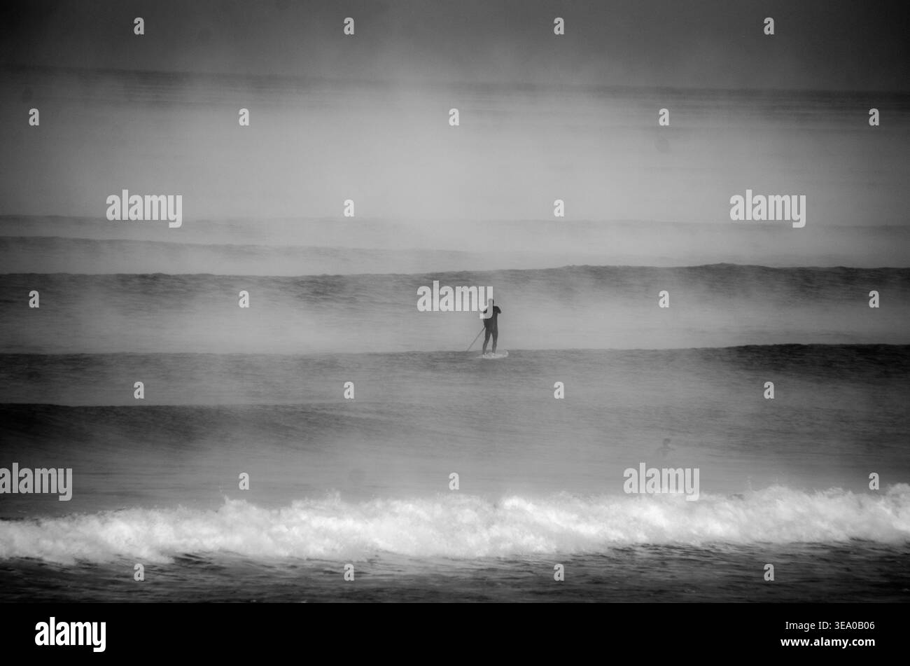Vista di un surfista solitario che si staglia contro l'orizzonte nebbioso, cavalcando un'onda sul mare scuro sotto un cielo coperto, Hossegor, Francia. Foto Stock
