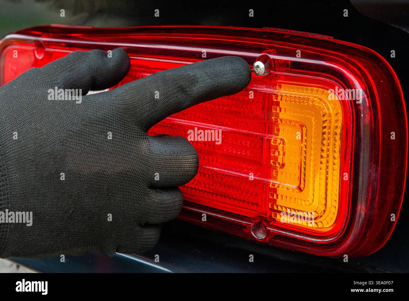 Primo piano di un dito con i guanti rivolto verso la vite di fissaggio della luce posteriore di un veicolo. Dimostrazione della diagnostica o della riparazione. Foto Stock