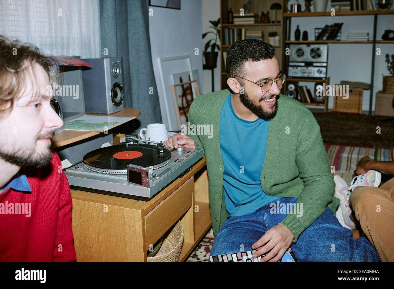 Diversi uomini ascoltano il vinile record durante la riunione sociale domestica Foto Stock