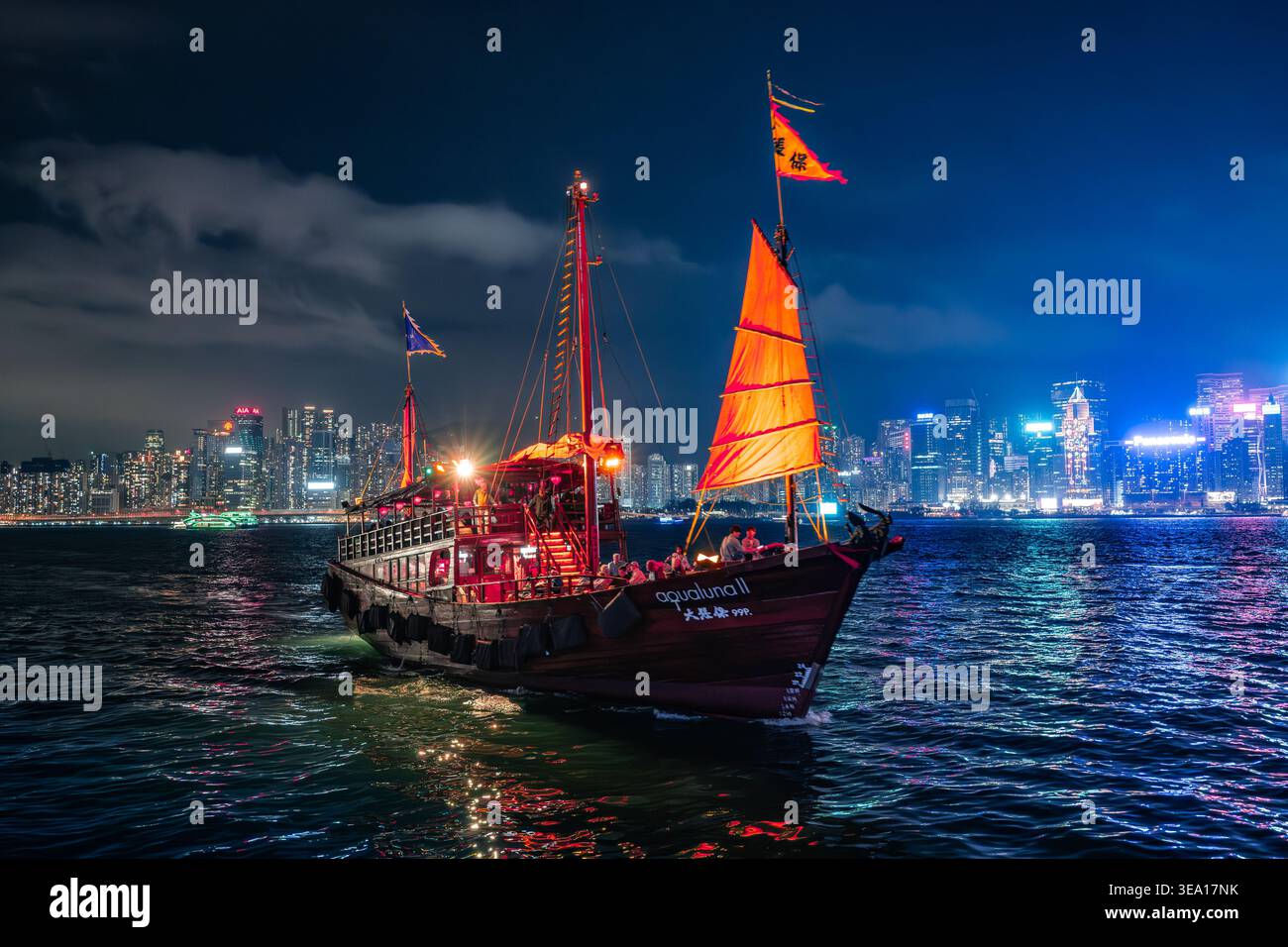 L'Aqua Luna II naviga di notte sul Victoria Harbour di Hong Kong durante lo spettacolo di laser Symphony of Lights con skyline illuminato sullo sfondo. Foto Stock