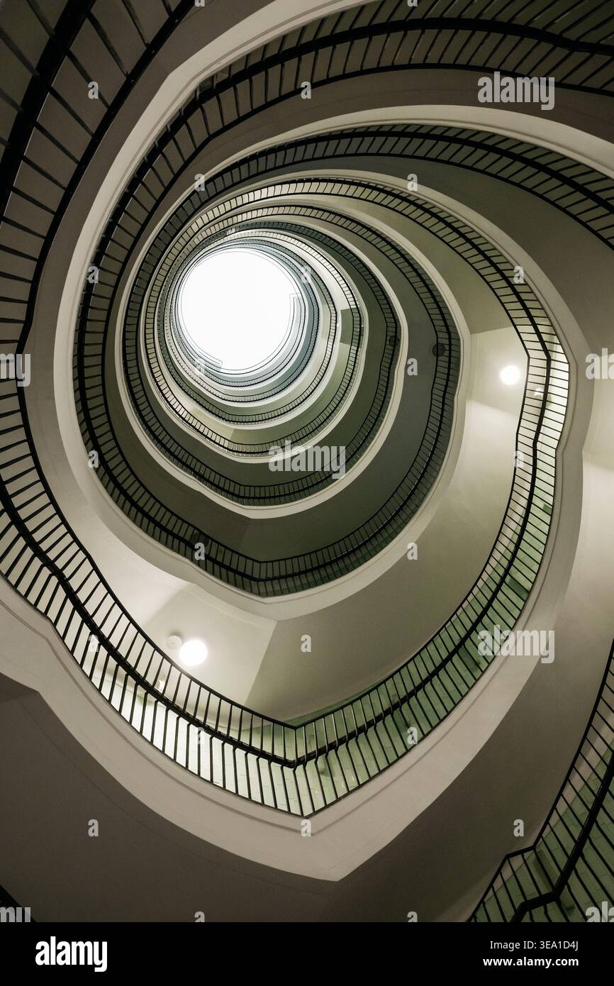 Prospettiva verticale di una scala a chiocciola. Ripresa ad angolo basso di una scala tortuosa con ringhiere scure e un lucernario luminoso. Foto Stock