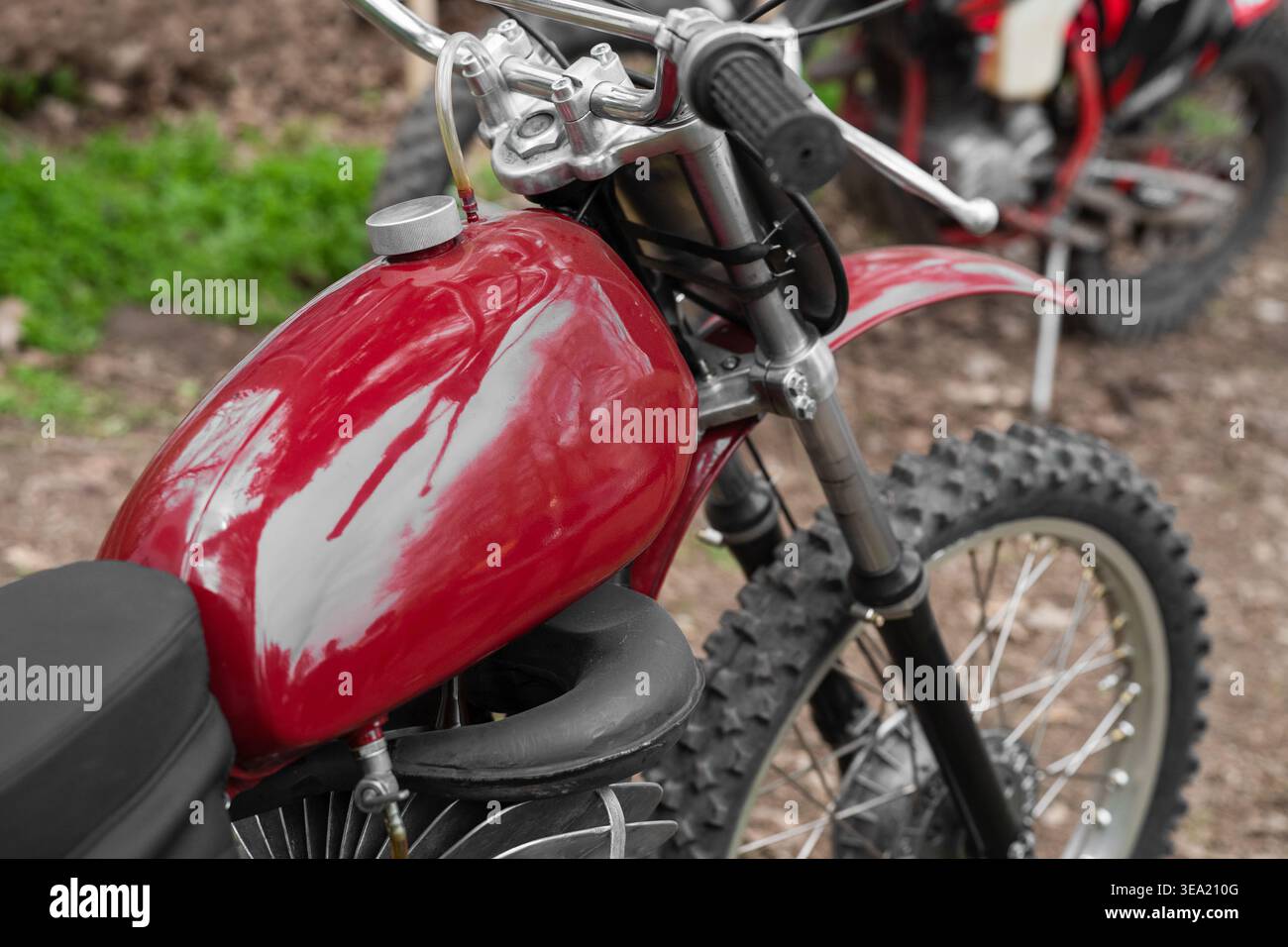 Moto da motocross rossa d'epoca con serbatoio del carburante lucido e pneumatici fuoristrada sospesi parcheggiati su una pista sterrata, concetto di moto da motocross retrò. Foto Stock
