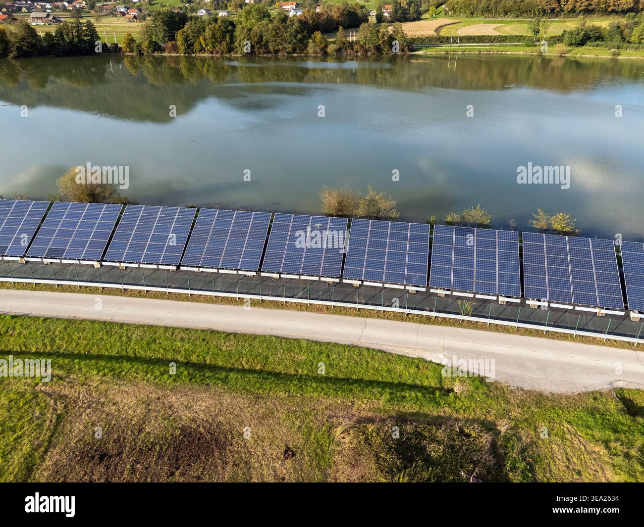 I pannelli solari si estendono lungo una riva del fiume, producendo energia pulita in un ambiente naturale sotto cieli limpidi. Foto Stock