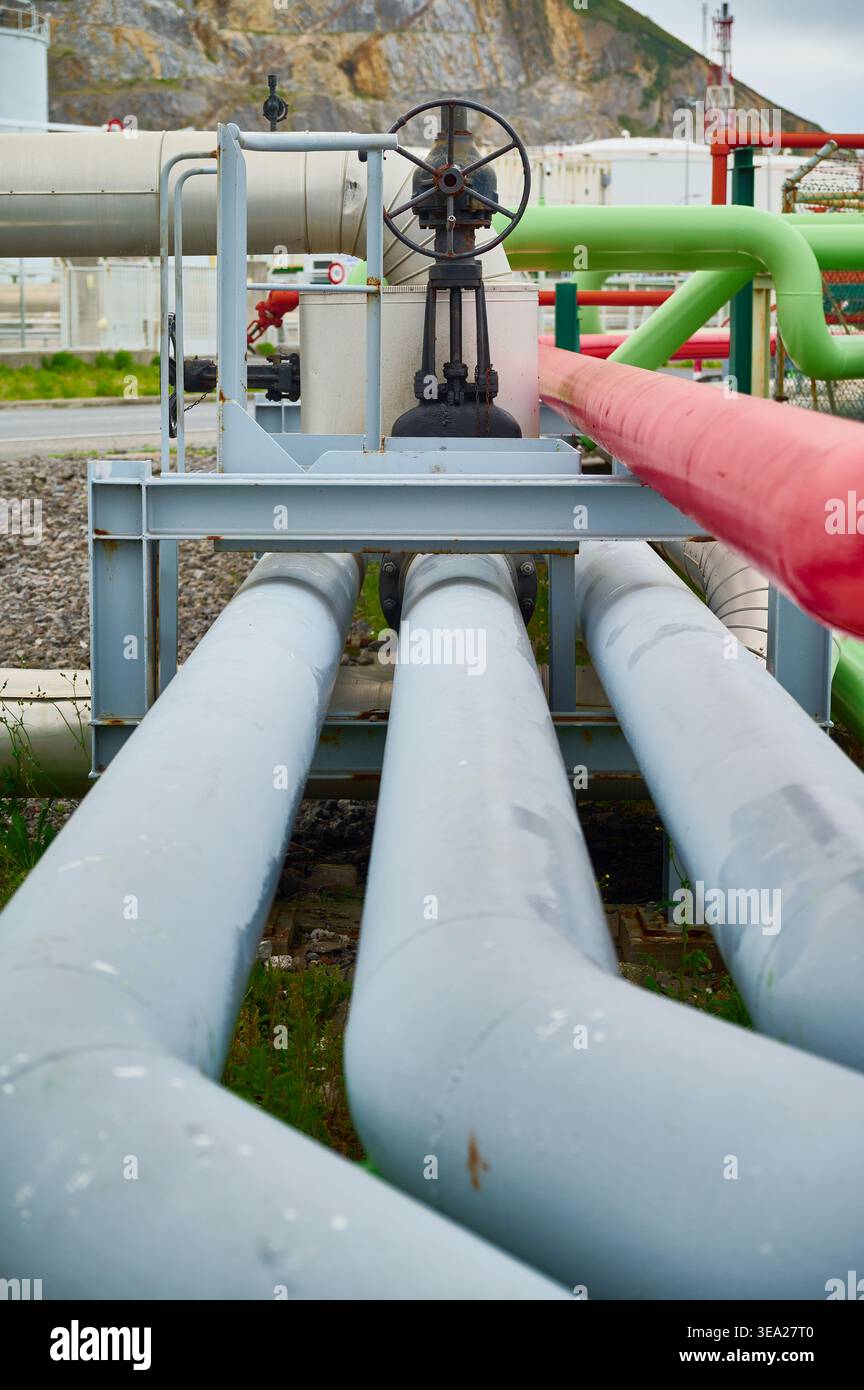 Tubazioni interconnesse con vari colori e una grande valvola manuale in un impianto industriale, che mostra l'infrastruttura energetica Foto Stock
