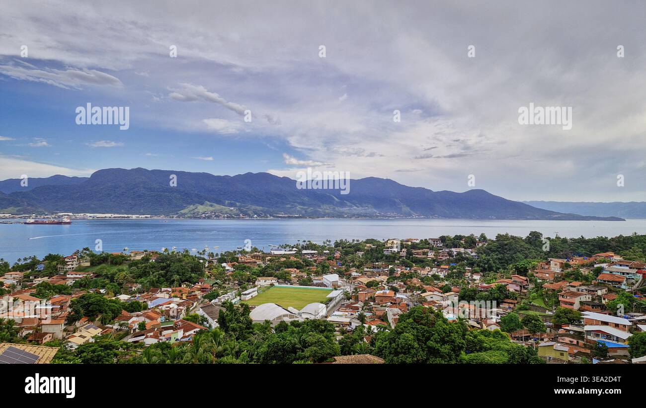 Un ampio orizzonte con mare blu, case affascinanti e vegetazione verde sotto un cielo limpido e soleggiato, che trasmette calma e leggerezza - Immagine stock catturata con smartphone