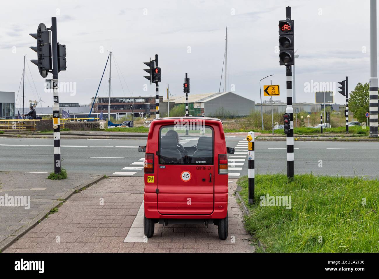 Amsterdam, Paesi Bassi, 11 aprile 2026. Una microcar rossa olandese Canta LX per conducenti disabili si è fermata a un semaforo rosso su un incrocio di pista ciclabile. Foto Stock