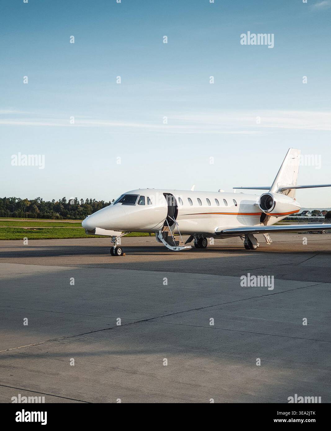 Jet privato con porta aperta sul grembiule dell'aeroporto al tramonto. Vista anteriore di tre quarti del business jet parcheggiato su un asfalto con scale aperte. Foto Stock