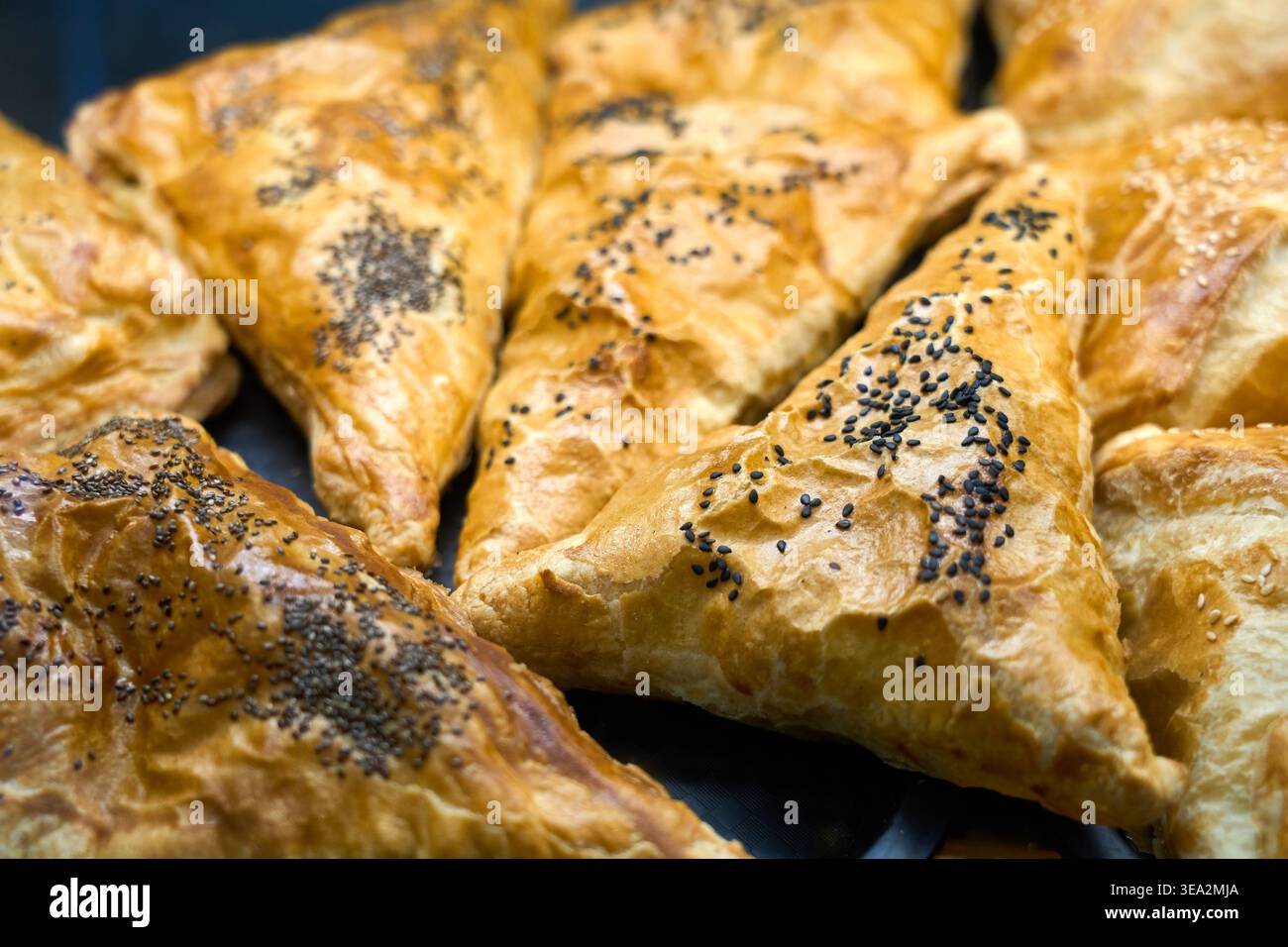 Pasticcini triangolari appena sfornati con semi di sesamo nero. Crosta dorata salata o salata. Samsa orientale tradizionale. Foto Stock