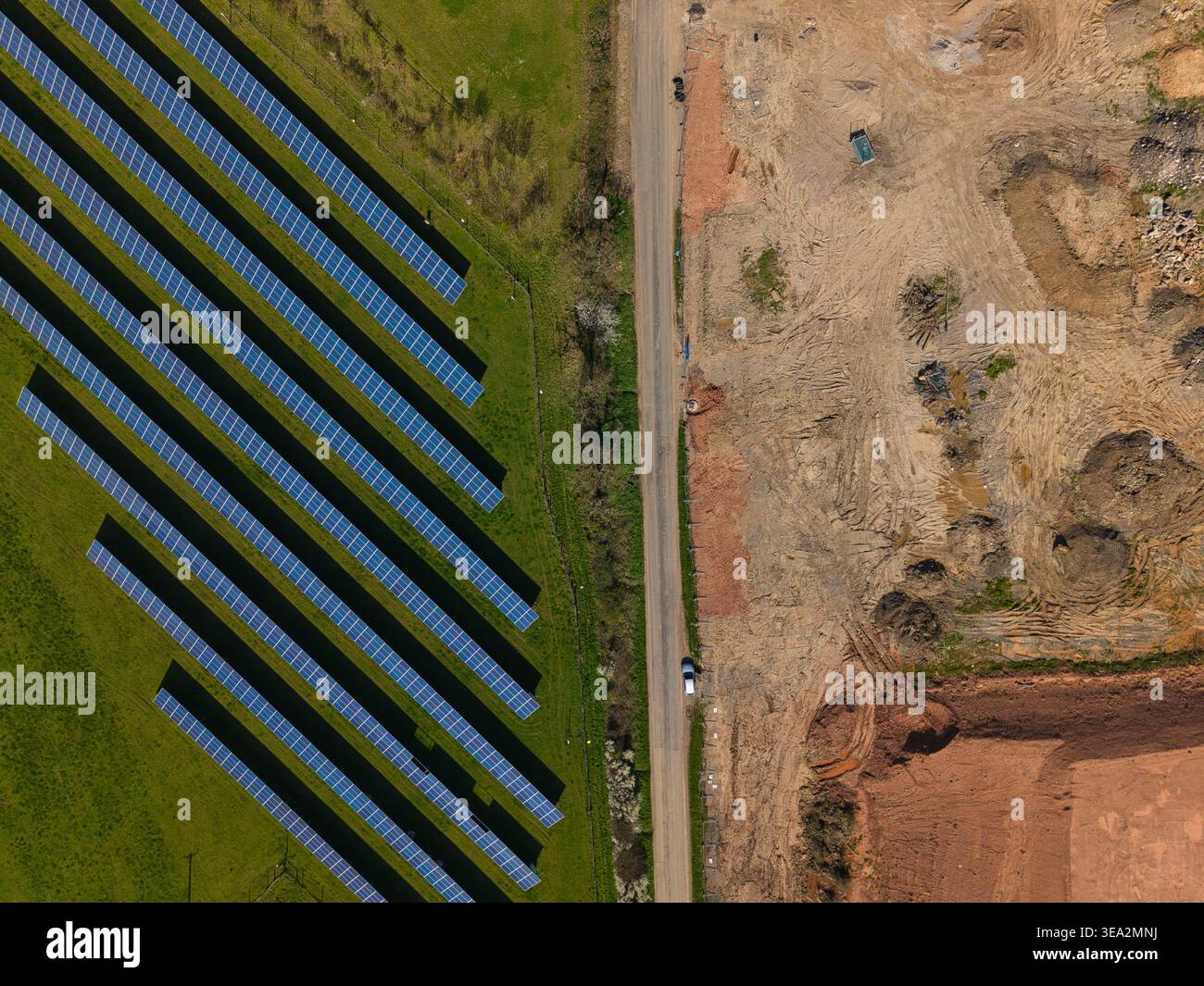 Vista aerea di file di pannelli solari blu su erba verde accanto a un cantiere in terra marrone separato da una strada stretta a Coalville, Inghilterra, Unit Foto Stock