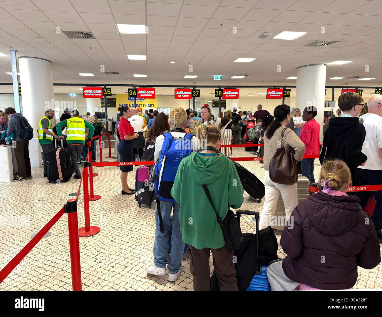 Grande folla di passeggeri in attesa in lunghe file ai banconi di check-in dell'aeroporto di Faro per i voli Jet2.com con valigie e zaini, ritardi di viaggio EES UE - Immagine stock catturata con smartphone