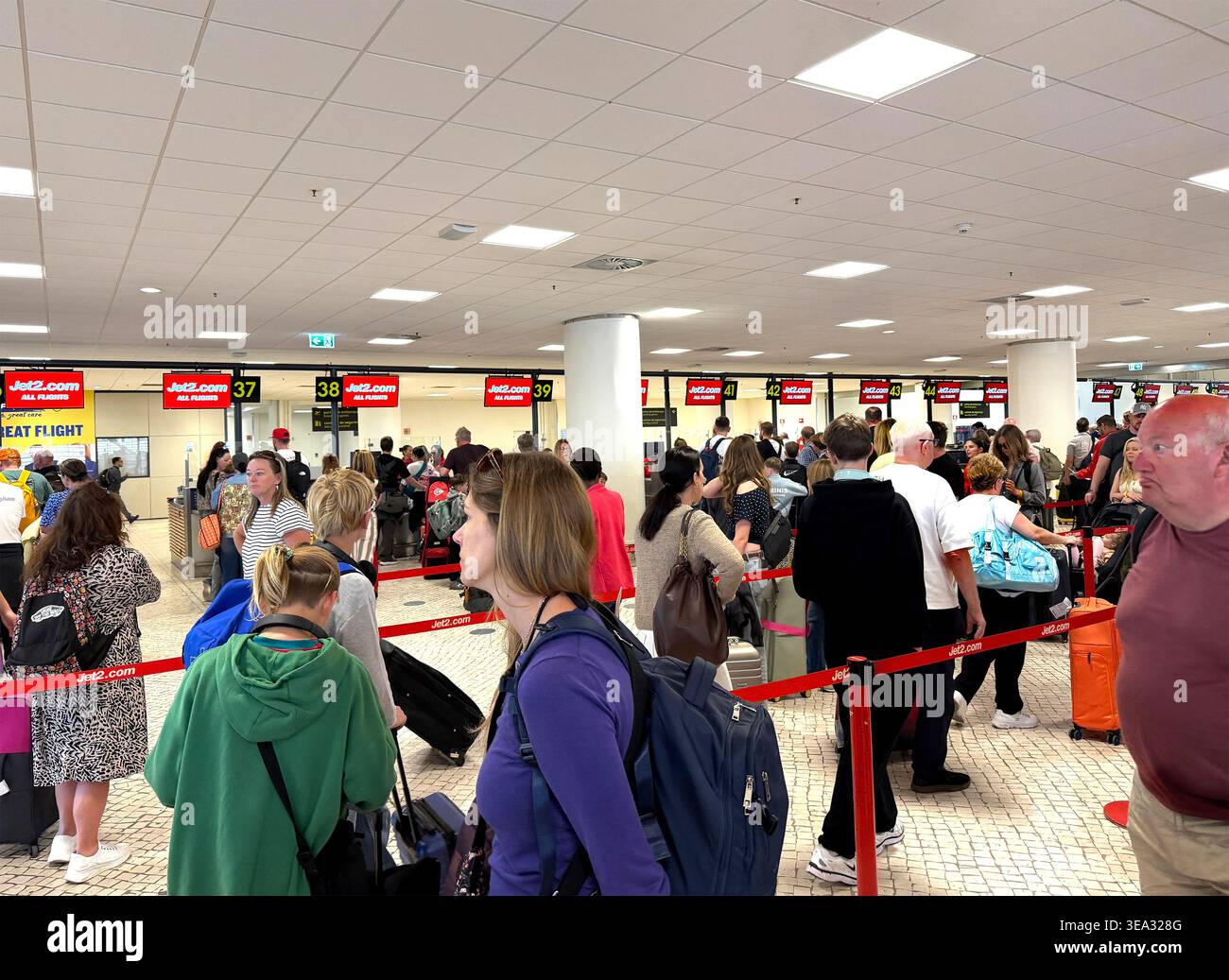 Grande folla di passeggeri in attesa in lunghe file ai banconi di check-in dell'aeroporto di Faro per i voli Jet2.com con valigie e zaini, ritardi di viaggio EES UE - Immagine stock catturata con smartphone