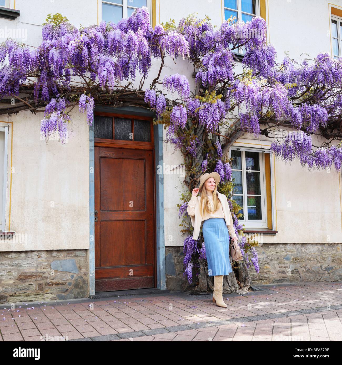 Donna che posa per casa con fiori di glicine viola, atmosfera di viaggio e bellezza stagionale. Foto Stock
