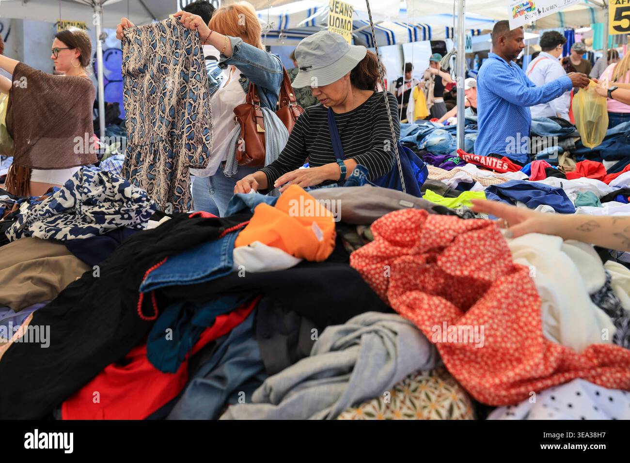 Gli acquirenti che ispezionano l'abbigliamento vintage al mercato delle pulci di porta Portese. Roma, Italia - 19 aprile 2026: Gli acquirenti vengono catturati mentre esaminano attentamente abiti e camicie a motivi geometrici tra pile di abiti di seconda mano in una bancarella del mercato di porta Portese. L'immagine riflette la tipica ricerca domenicale di pezzi unici e moda a basso costo, documentando la vitalità sociale ed economica del più famoso spazio di vendita all'aperto di Roma. Roma RM Italia Copyright: XGennaroxLeonardix Foto Stock