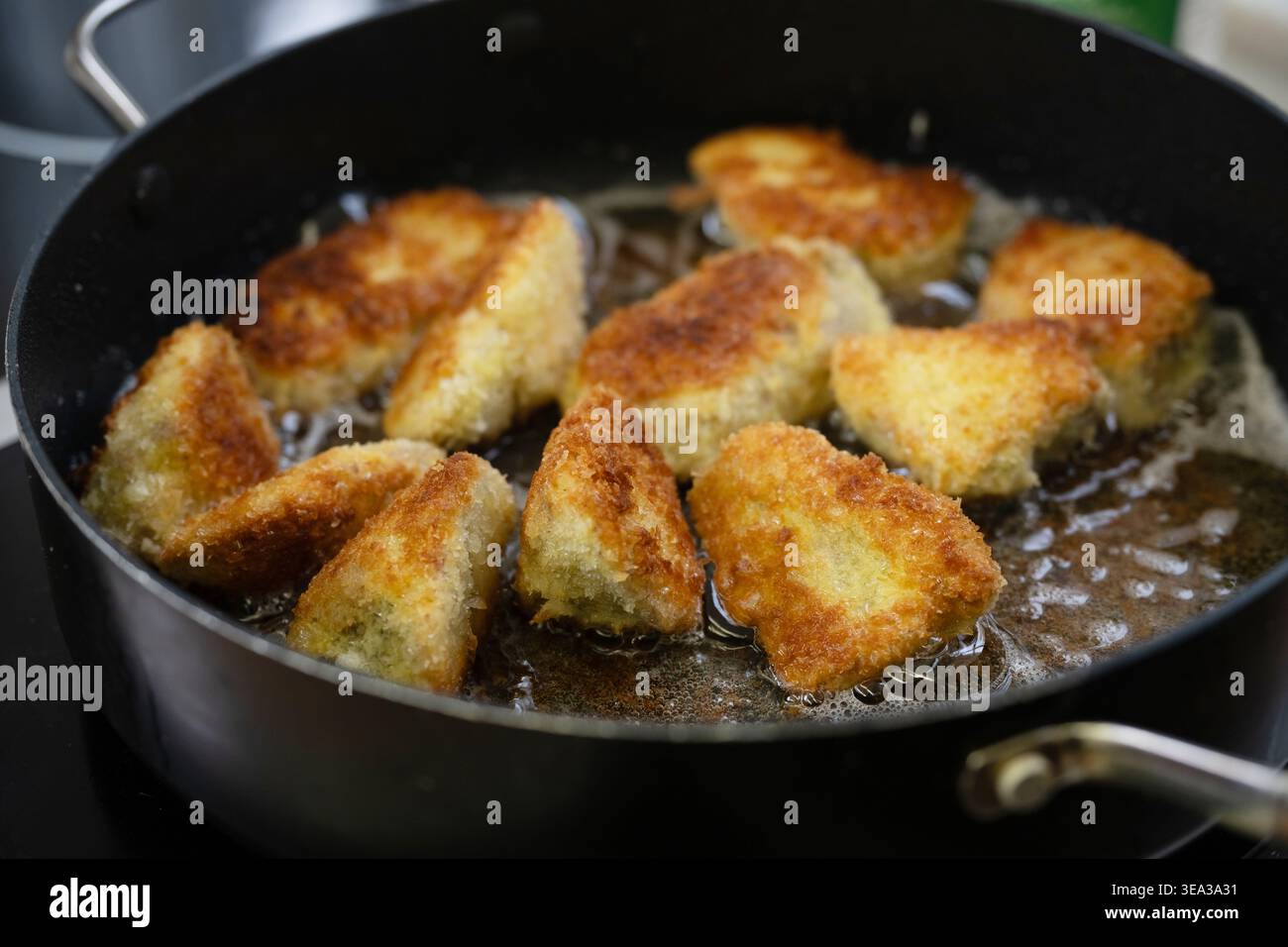 Friggendo pezzi di carne o pesce impanati in olio caldo in una padella nera, diventano ancora più croccanti grazie al pangrattato panko giapponese, alla messa a fuoco selezionata, stretto Foto Stock