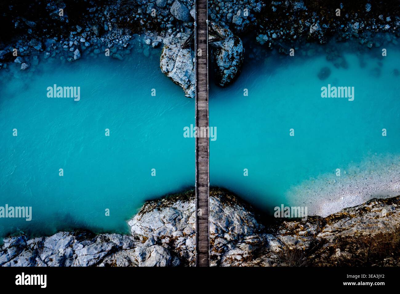 Vista aerea di una stretta passerella in legno che attraversa un vivace fiume turchese con sponde rocciose e acque cristalline in Slovenia. Foto Stock