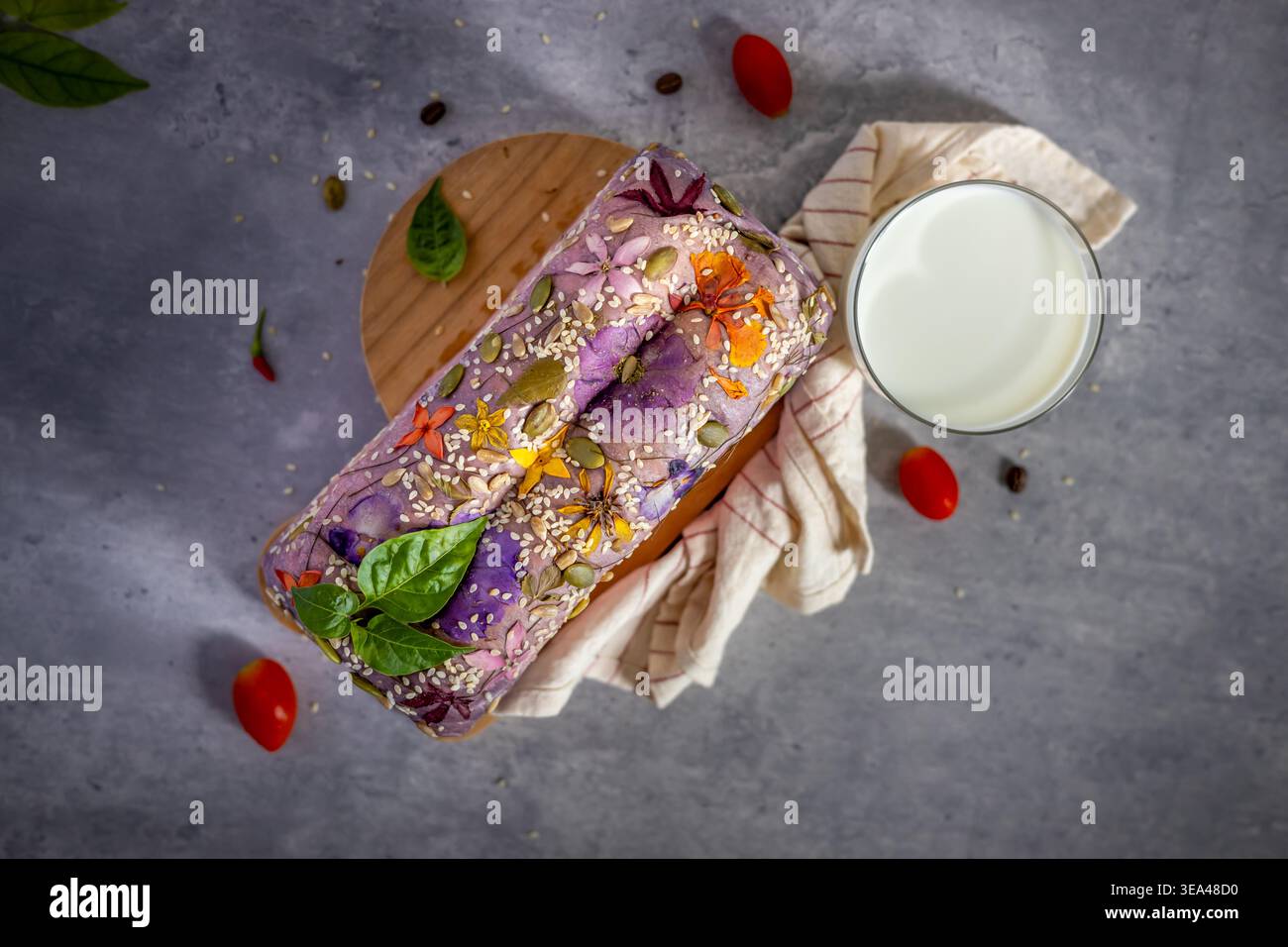 Vista dall'alto di una pagnotta di pane con fiori commestibili, sgargiante, gelsomino dell'india occidentale, rose e cereali, pane fatto in casa, mangiare sano. Primo piano. Foto Stock