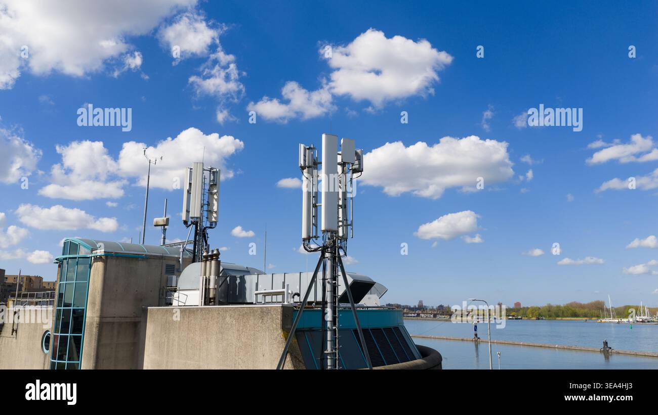 Vista aerea delle antenne di telecomunicazione e delle torri 5G in un edificio moderno a Zuider IJdijk che si affaccia sull'acqua sotto un cielo blu luminoso con nuvole Foto Stock