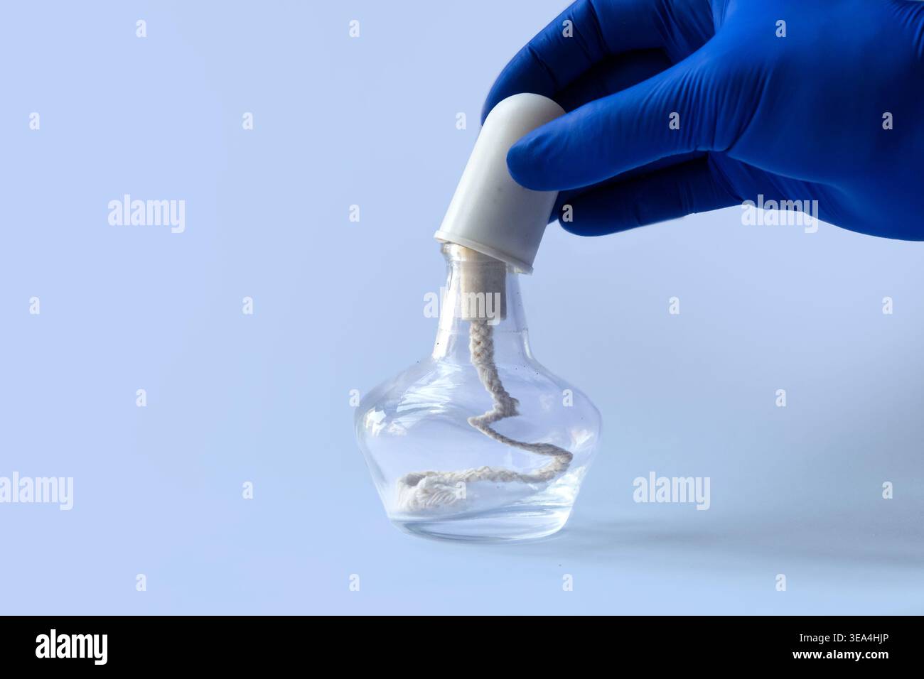 Mano con guanti per rimuovere il tappo da una lampada bruciatore in vetro con alcool in laboratorio. Foto Stock
