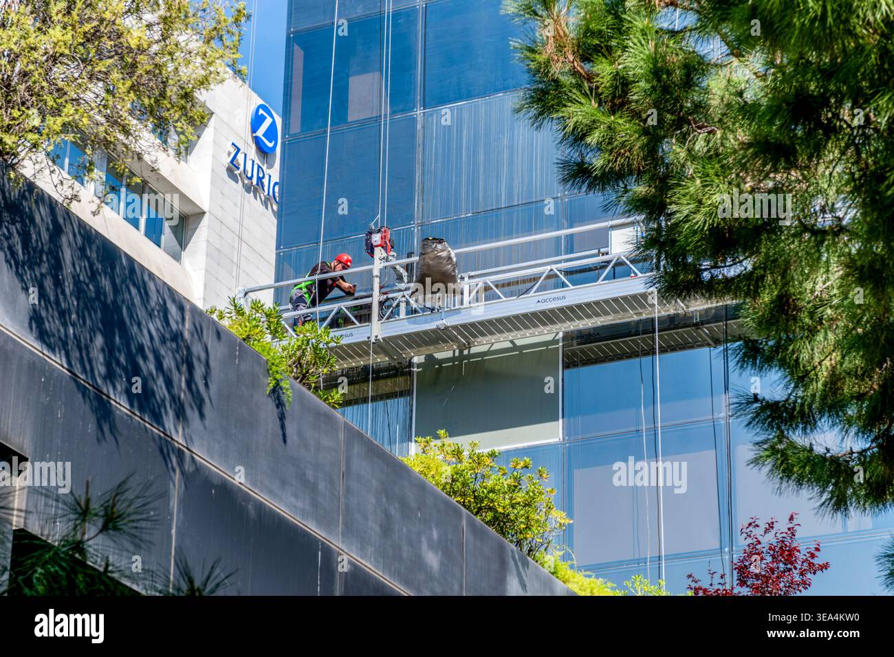 Lavavetri che lavora su una piattaforma sospesa su un moderno edificio in vetro, addetto al servizio di manutenzione con attrezzature di sicurezza Foto Stock