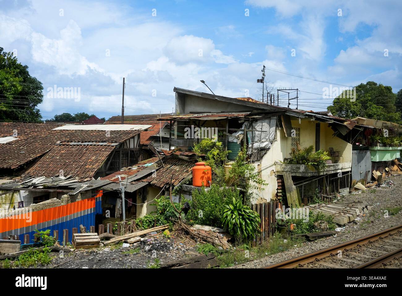 Una vista delle case improvvisate e degli affollati insediamenti urbani costruiti pericolosamente vicino a una linea ferroviaria sotto un cielo blu. La scena raffigura la povertà urbana A. Foto Stock