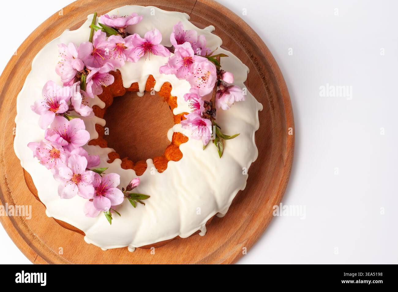 Una torta ben decorata con un anello di fiori rosa vibranti e una glassa bianca liscia, presentata su una tavola di legno Foto Stock