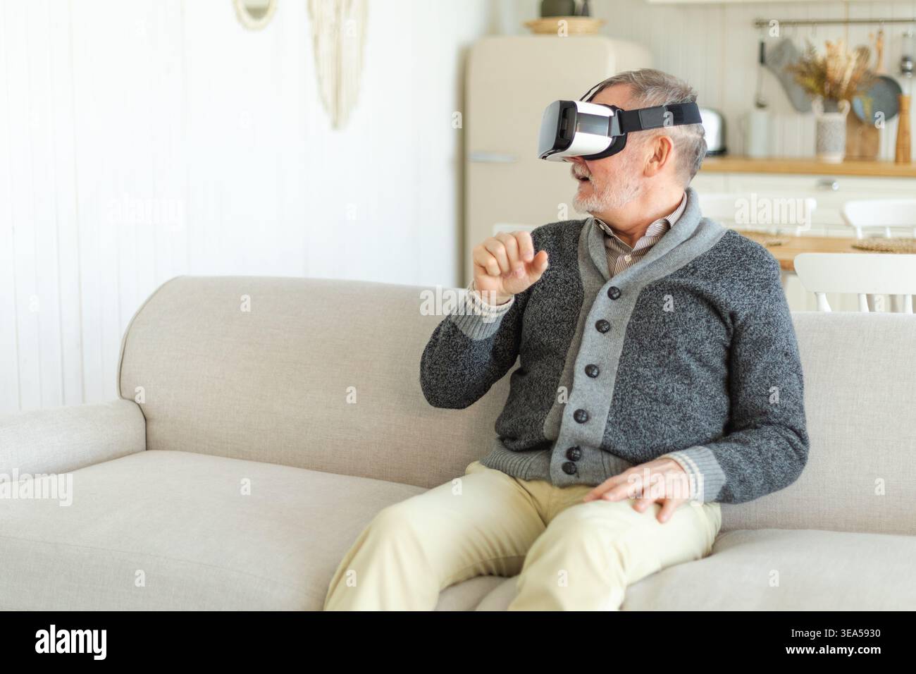 Un uomo anziano entusiasta indossando occhiali VR in realtà virtuale metaverse a casa. Nonno che tocca l'aria durante l'esperienza di realtà virtuale su casco per realtà virtuale. Videogame di simulazione ad alta tecnologia Foto Stock
