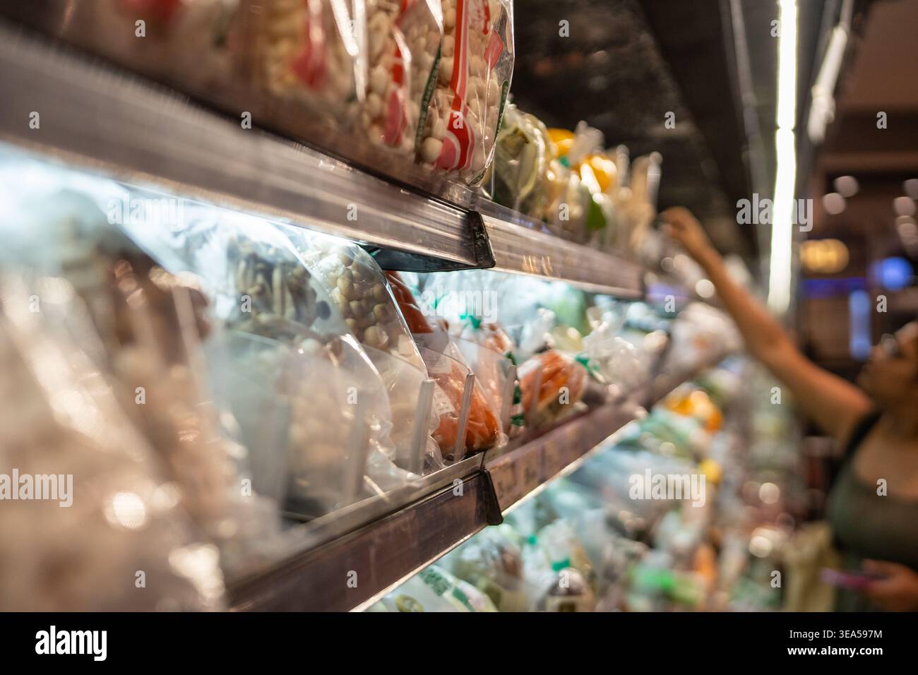Cliente che prende il pacco dagli scaffali del frigorifero pieni di prodotti alimentari freschi nel negozio in Thailandia Foto Stock