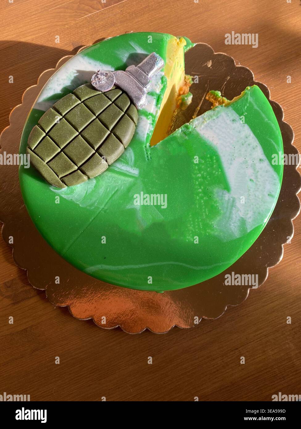 Torta verde da festa con decorazione a forma di granata, parzialmente affettata, posta su un tavolo di legno con luce naturale. torta, dessert, torta di festa Foto Stock