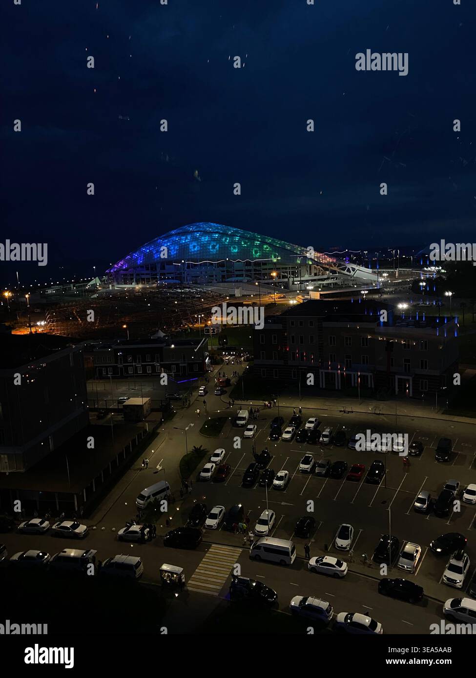Sochi, Russia- maggio 31 2021: Paesaggio urbano notturno con stadio moderno illuminato e parcheggio con auto e persone Foto Stock
