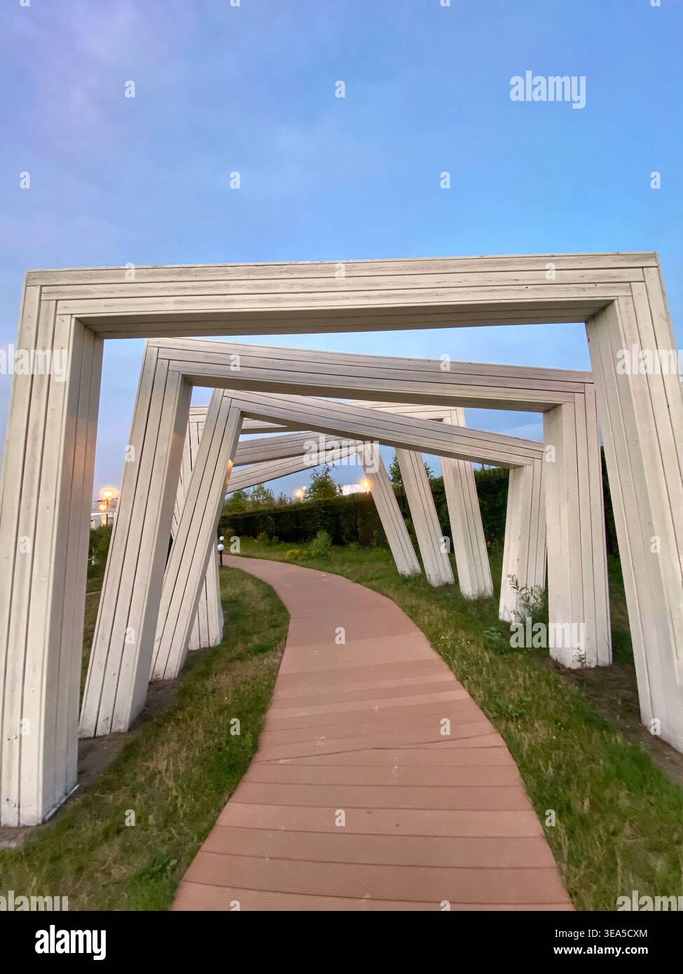 Moderne cornici architettoniche in legno che formano una prospettiva geometrica del percorso in un parco al tramonto - Immagine stock catturata con smartphone