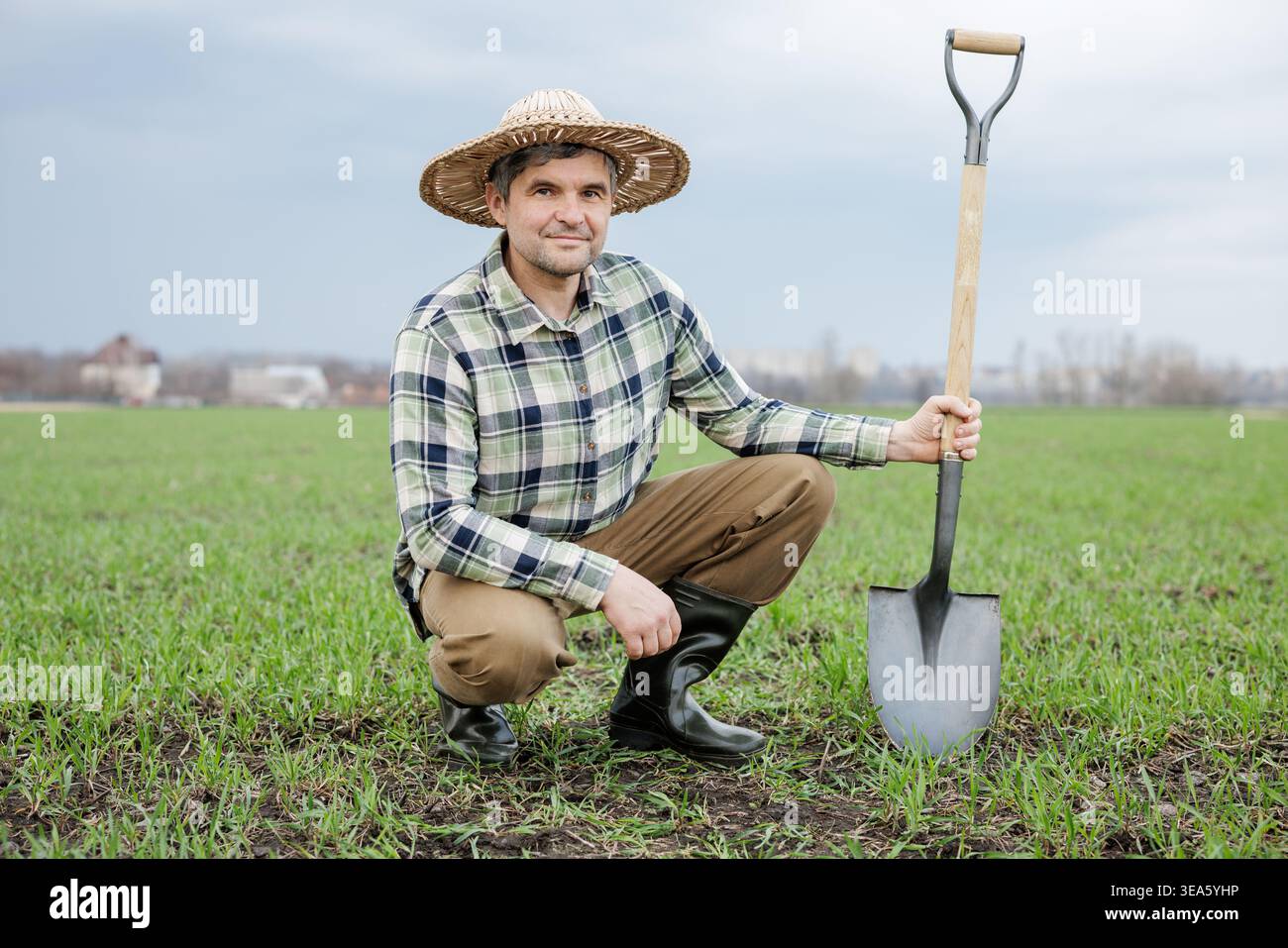 Agricoltore inginocchiato sul campo agricolo con pala durante la preparazione primaverile del terreno. Concetto di agroalimentare, coltivazione delle colture e agricoltura sostenibile Foto Stock