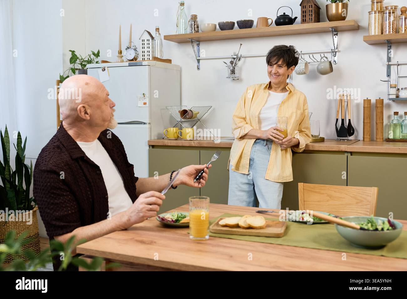Una coppia di anziani affettuosa condivide una colazione gioiosa, assaporando la compagnia degli altri e il cibo delizioso. Foto Stock